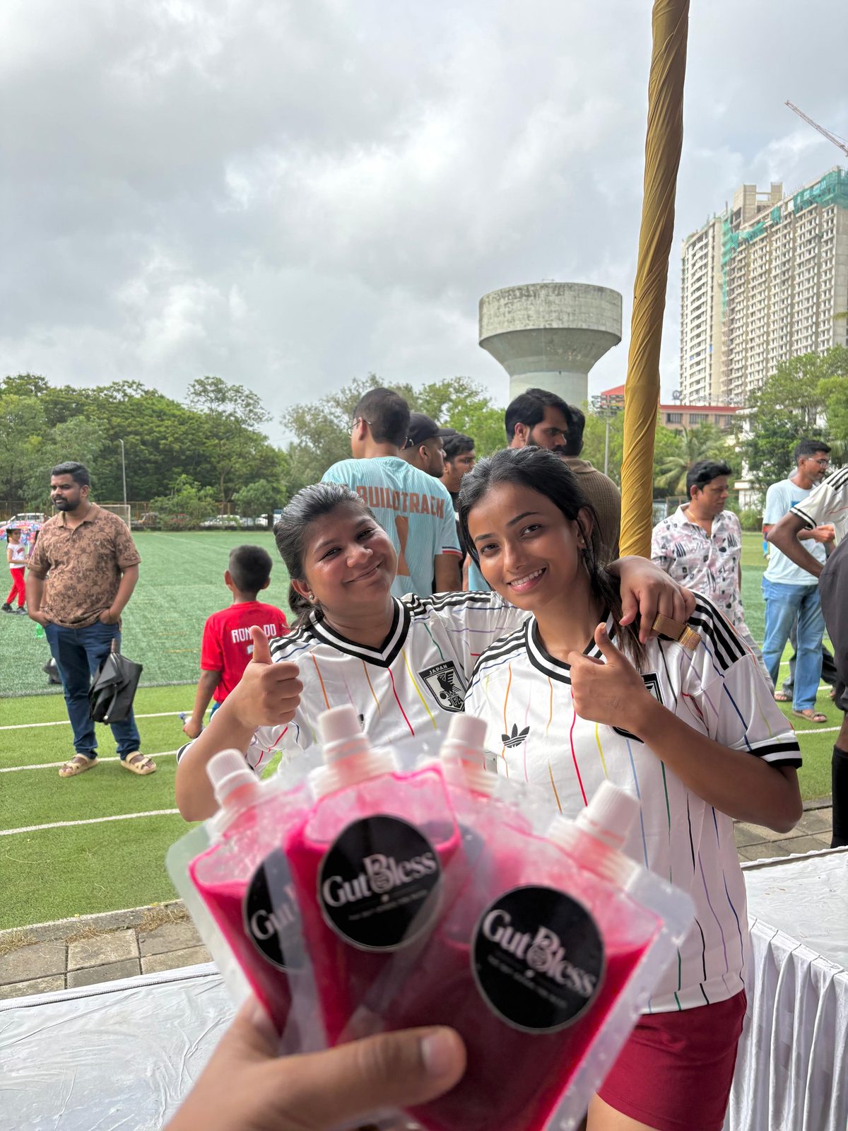 Two happy customers in jerseys giving a thumbs up while holding GutBless juice pouches at a sports event