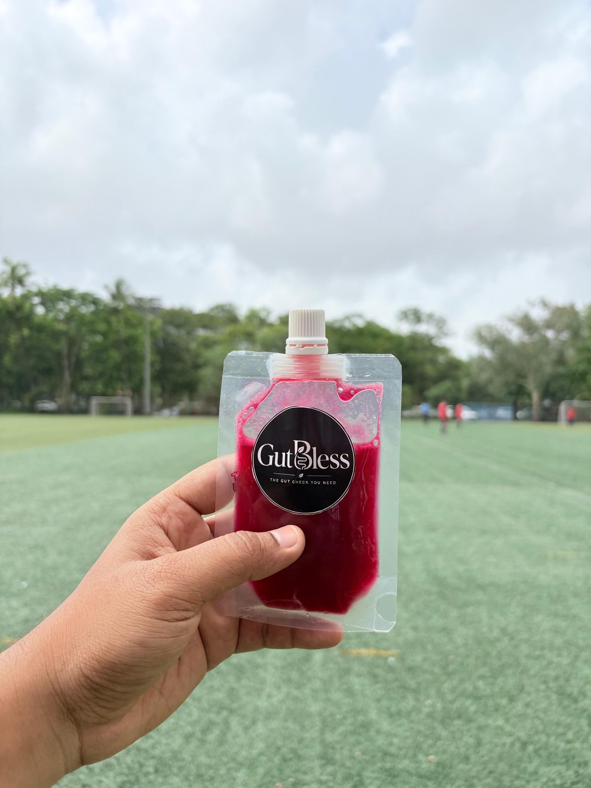A GutBless dragon fruit juice pouch held up on a football field